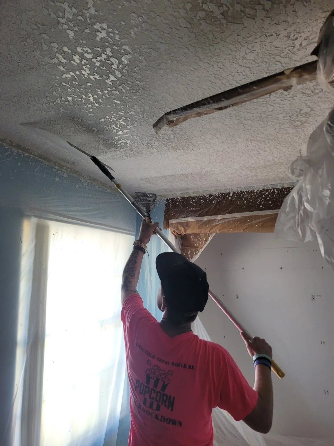 Worker using a long knockdown blade on newly applied ceiling texture
